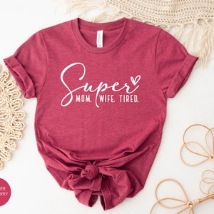 May include: A heather raspberry t-shirt with the text "Super Mom. Wife. Tired." in white lettering with a small heart.