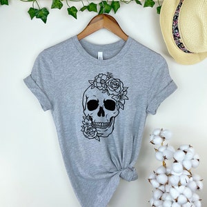 Peut inclure: T-shirt gris avec un motif de cr&acirc;ne noir et blanc avec des fleurs sur le dessus du cr&acirc;ne.