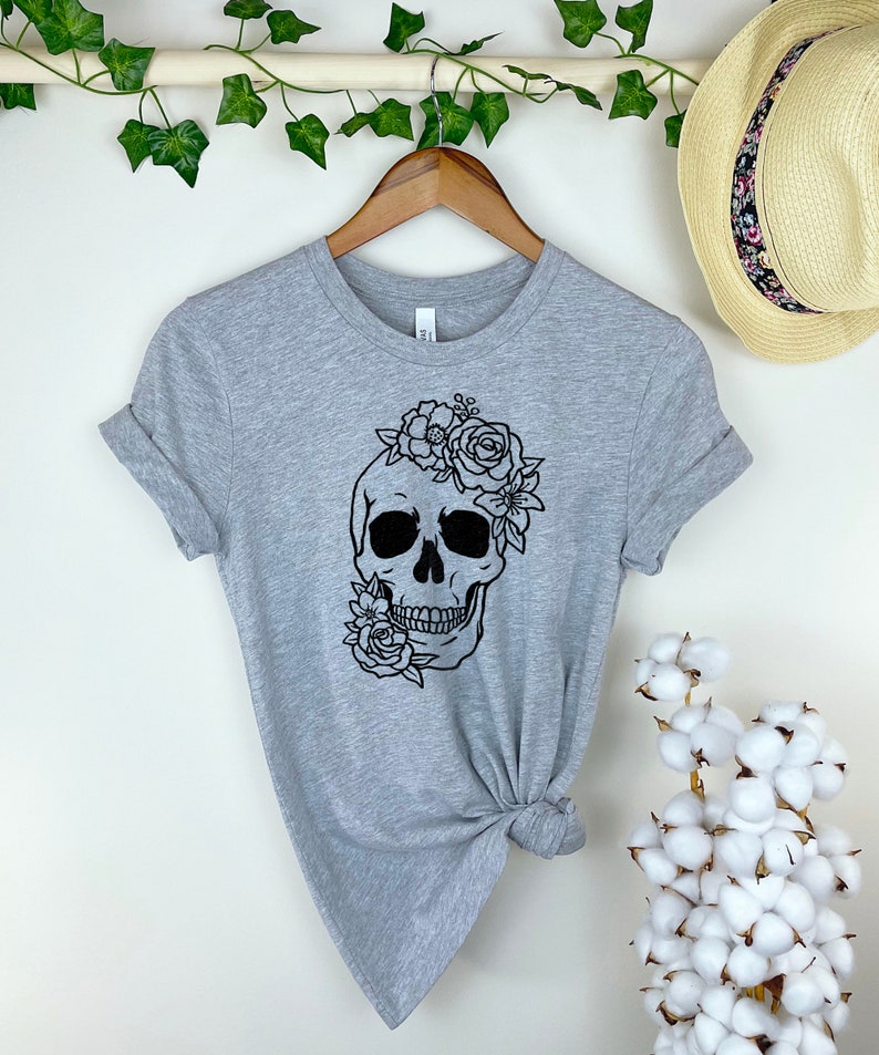 Peut inclure: T-shirt gris avec un motif de cr&acirc;ne noir et blanc avec des fleurs sur le dessus du cr&acirc;ne.