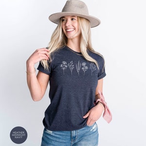 May include: A heather midnight navy t-shirt with a white floral design. The shirt is being worn by a person with blonde hair and a grey hat.