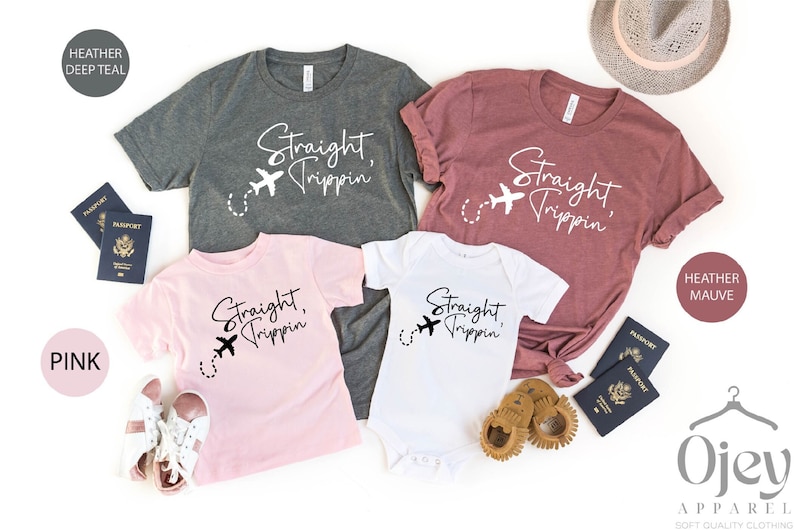 May include: A set of four t-shirts with the text "Straight, Trippin'" and a small airplane graphic. The shirts are in different colors: heather deep teal, heather mauve, pink, and white. The shirts are arranged on a white background with passports and other travel accessories.