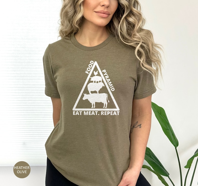 May include: A green t-shirt with a white graphic of a food pyramid featuring a cow, sheep, pig, and chicken. The text "Food Pyramid" is written on the right side of the triangle and "Eat Meat. Repeat" is written below the triangle.
