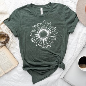 Puede incluir: Una camiseta verde con un gr&aacute;fico de margarita blanca. La camiseta est&aacute; anudada en la parte delantera.