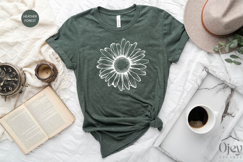 Puede incluir: Una camiseta verde con un gr&aacute;fico de margarita blanca. La camiseta est&aacute; anudada en la parte delantera.