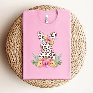 May include: Pink t-shirt with a floral design featuring a leopard print Easter bunny.