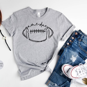 Peut inclure: Un t-shirt gris chin&eacute; avec un graphique noir d'un ballon de football et le texte "game day".