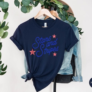 May include: Navy blue t-shirt with the text "Stars and Stripes" in blue with red glitter stars.