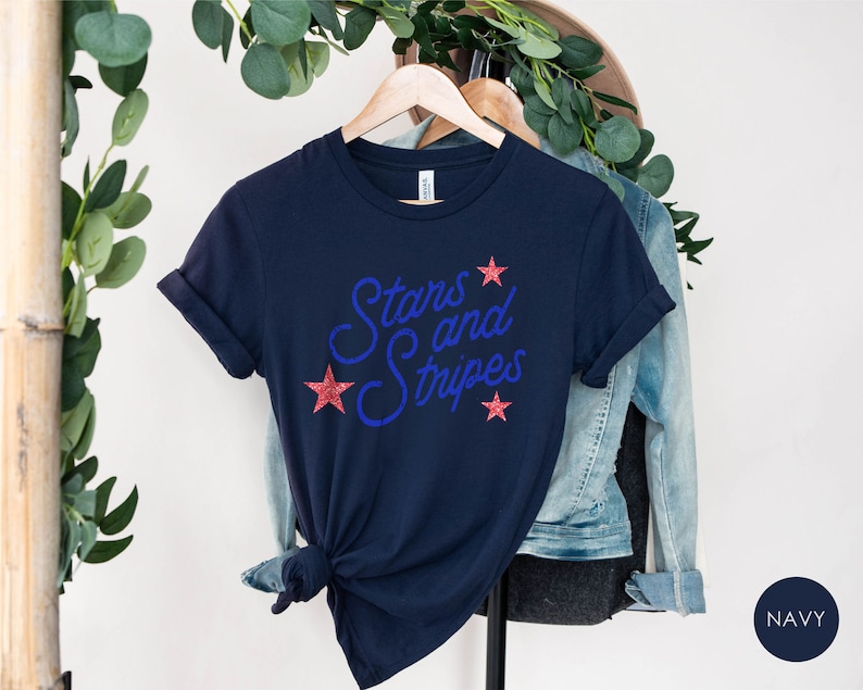 May include: Navy blue t-shirt with the text "Stars and Stripes" in blue with red glitter stars.