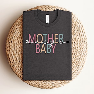 Puede incluir: Una camiseta gris oscuro con el texto "Madre de un beb&eacute;" en letras de colores. El texto est&aacute; en un estilo moderno y manuscrito.
