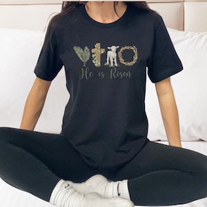 May include: A black t-shirt with a graphic design of a cross, a lamb, and a crown of thorns. The text "He is Risen" is printed below the graphic.