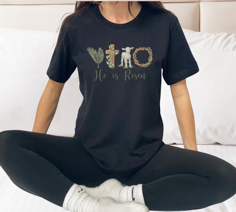 May include: A black t-shirt with a graphic design of a cross, a lamb, and a crown of thorns. The text "He is Risen" is printed below the graphic.