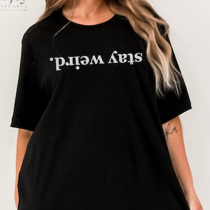 May include: Black oversized t-shirt with the text "Stay Weird." printed in white.
