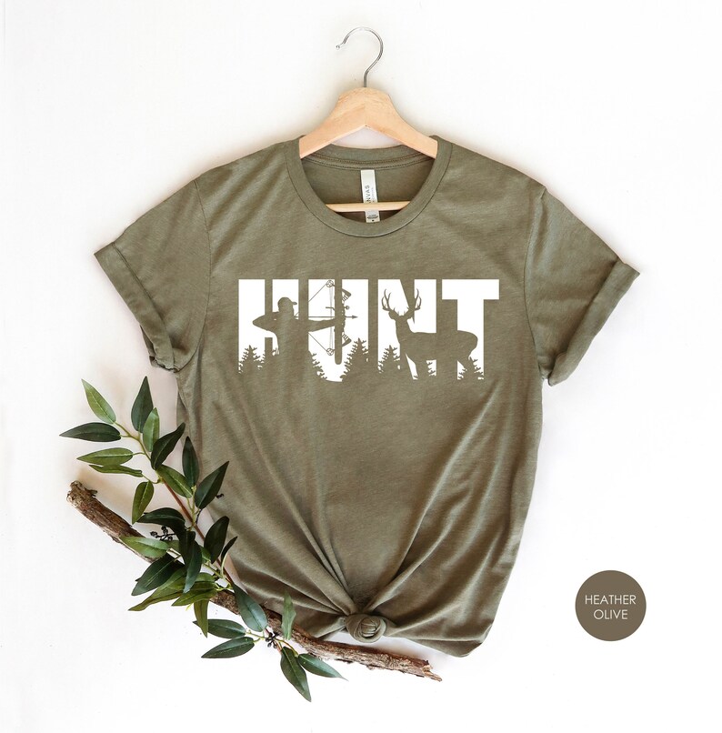 May include: A green t-shirt with the word "HUNT" in white text. The letters are outlined with a silhouette of a hunter with a bow and arrow and a deer.
