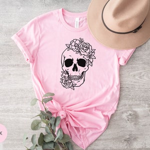 Peut inclure: T-shirt rose avec une illustration noir et blanc d'un cr&acirc;ne surmont&eacute; de fleurs.