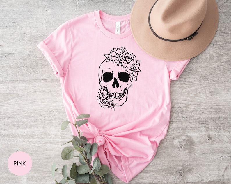 Peut inclure: T-shirt rose avec une illustration noir et blanc d'un cr&acirc;ne surmont&eacute; de fleurs.