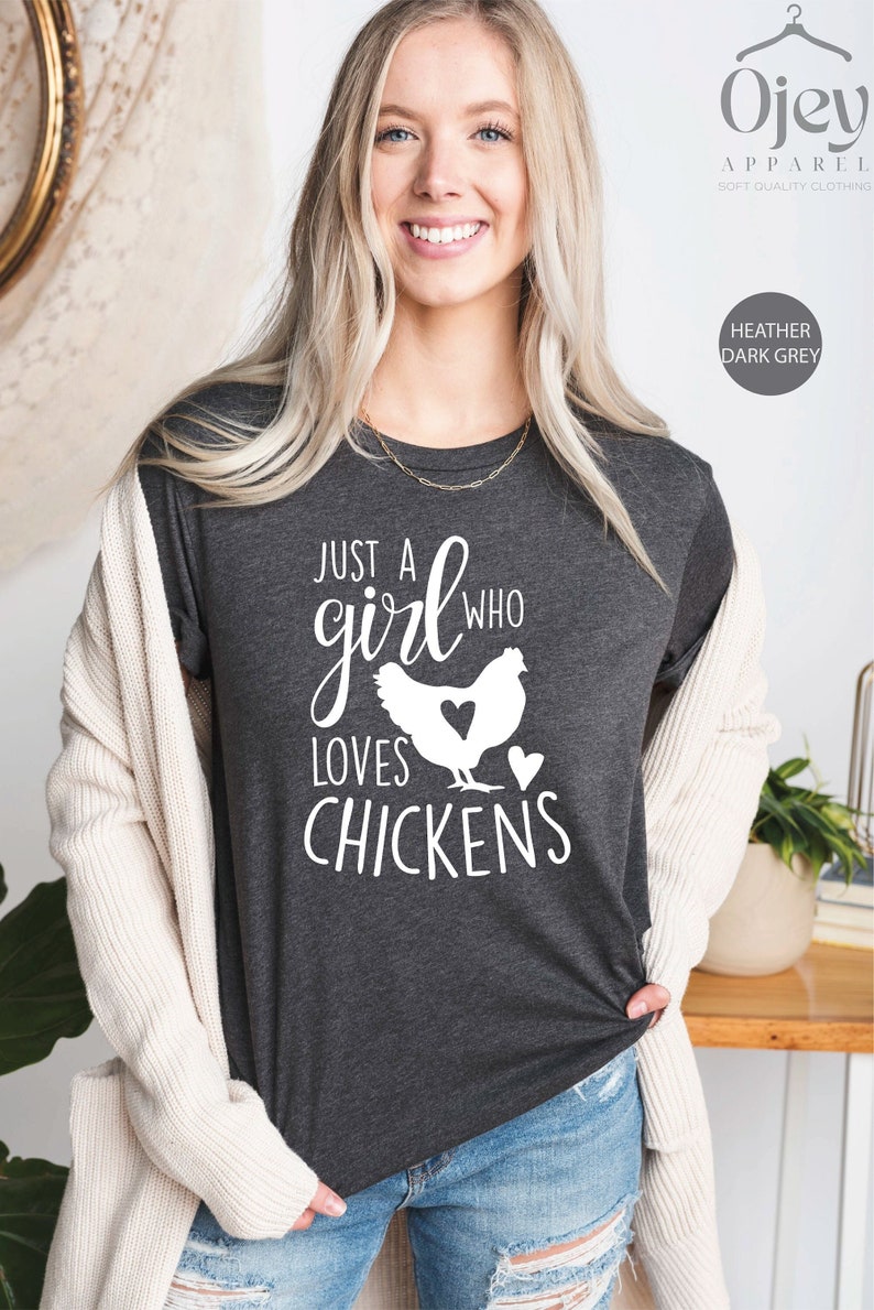 Puede incluir: Una camiseta gris oscuro jaspeada con el texto "Just a girl who loves chickens" y una silueta de una gallina con un coraz&oacute;n en el pecho.
