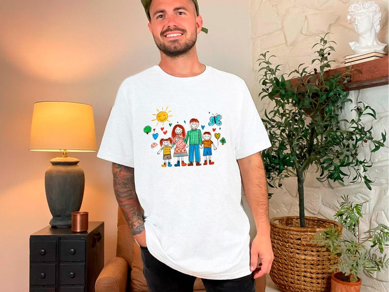 Peut inclure: T-shirt blanc avec une illustration color&eacute;e d'une famille avec un soleil, des c&oelig;urs et des papillons. L'illustration est dessin&eacute;e dans un style enfantin.