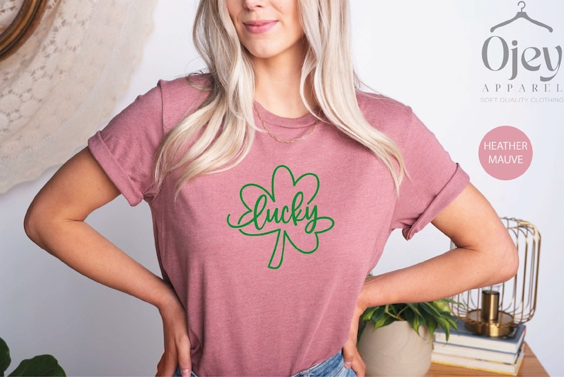 May include: A heather mauve t-shirt with a green four-leaf clover and the word "lucky" written in cursive.