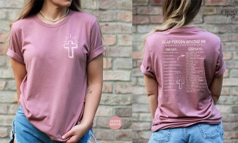 May include: A heather mauve t-shirt with a white cross and the text "Dear Person Behind Me" on the back. The text includes a list of phrases with "You Say" and "God Says" headings.