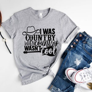 May include: Gray t-shirt with a black graphic that says "I was country when country wasn't cool". The graphic includes a cowboy hat and a guitar.