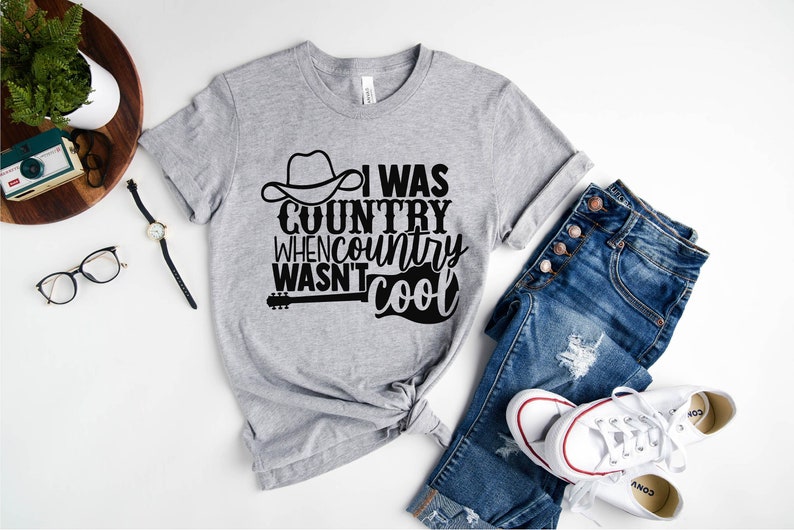 May include: Gray t-shirt with a black graphic that says "I was country when country wasn't cool". The graphic includes a cowboy hat and a guitar.