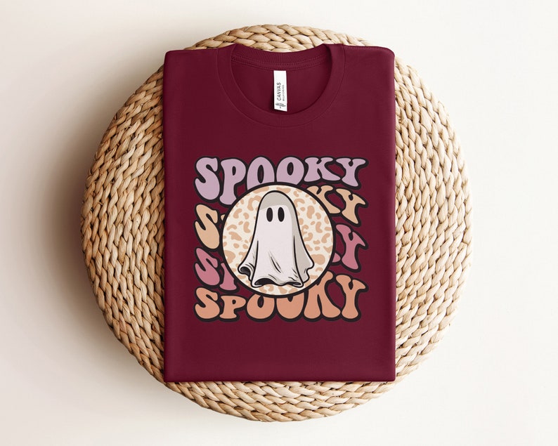 Puede incluir: Una camiseta color granate con un gr&aacute;fico retro de un fantasma en un c&iacute;rculo de estampado de leopardo. El texto "Spooky" est&aacute; escrito con una fuente ondulada alrededor del c&iacute;rculo.