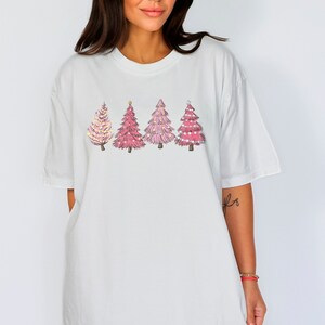 May include: White oversized t-shirt featuring a design of four pink Christmas trees with gold lights.