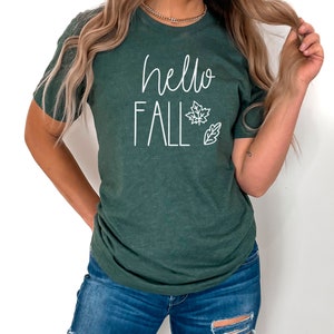 May include: A dark green t-shirt with the text "hello fall" in white lettering. The shirt features a white outline of a maple leaf and a small leaf.