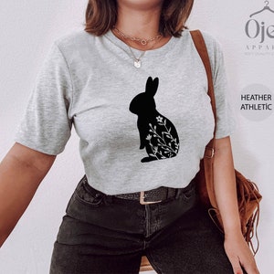 May include: A heather gray t-shirt with a black silhouette of a rabbit with floral details. The text "Ojev Apparel Soft Quality Clothing" and "Heather Athletic" are visible on the right side of the image.