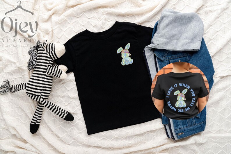 Puede incluir: Dos camisetas negras con un gr&aacute;fico de conejo colorido. Una camiseta tiene el texto "Me encanta cuando me llamas Hoppa" en la espalda.