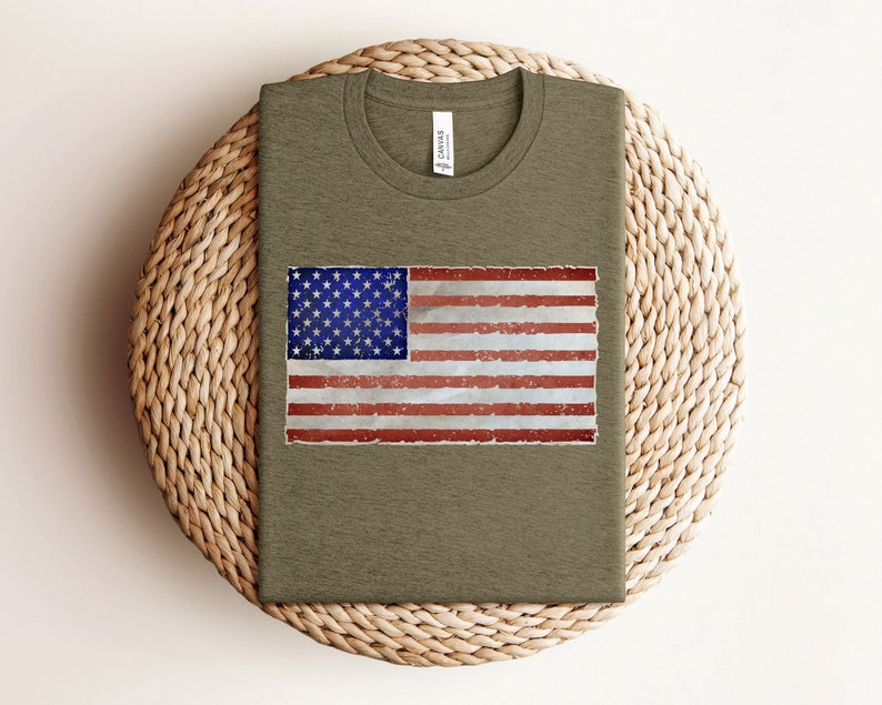 Pode incluir: Uma camiseta verde com um design de bandeira americana desbotada estampado na frente.