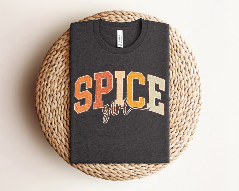 May include: A dark gray t-shirt with the text "SPICE girl" in a retro font with orange, yellow, and brown colors.