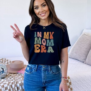 May include: A black t-shirt with the text "In My Mom Era" in colorful retro-style lettering.