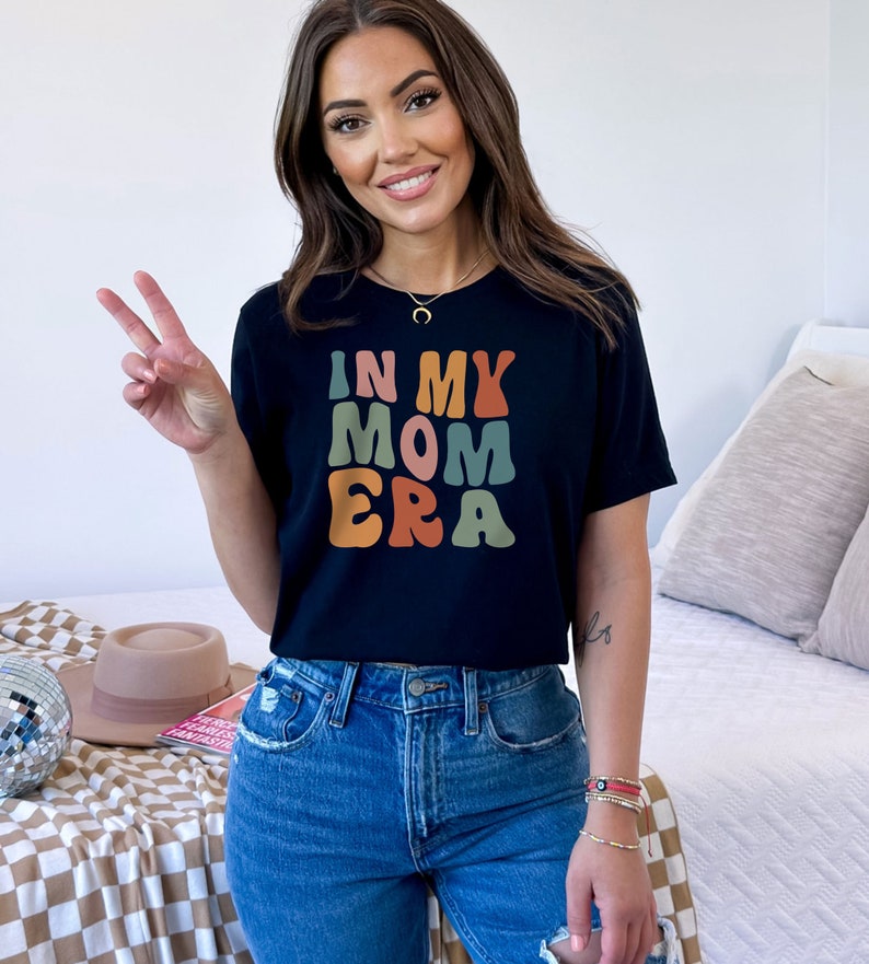 May include: A black t-shirt with the text "In My Mom Era" in colorful retro-style lettering.