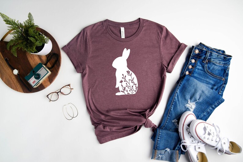 May include: A mauve t-shirt with a white silhouette of a rabbit with floral details.