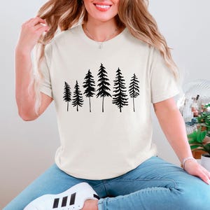 May include: A white t-shirt with a black silhouette of a group of pine trees printed on the front.