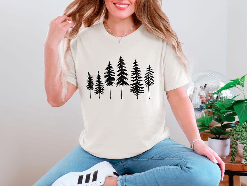May include: A white t-shirt with a black silhouette of a group of pine trees printed on the front.