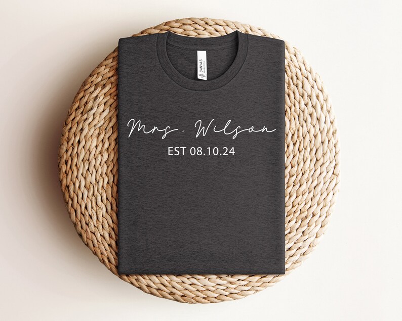 May include: A dark gray t-shirt with the text "Mrs. Wilson EST 08.10.24" in white.
