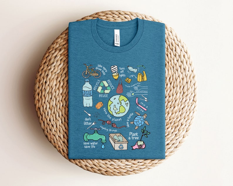 May include: A teal blue t-shirt with a graphic design of various ways to help save the planet. The graphic includes a bicycle, a lightbulb, a water bottle, a recycling symbol, a turtle, a tree, and the words "save the planet", "don't litter", "save water", "save life", "plant a tree", "recycle", "reduce", "reuse", "skip a straw", "turn off lights", "bike more drive less", "save a turtle", "upcycle things", and "volunteer".