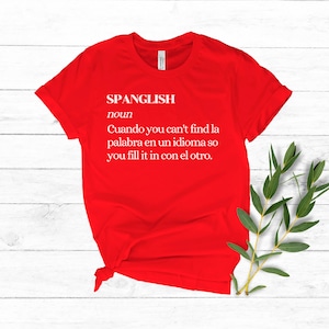 Puede incluir: Camiseta roja con texto blanco que dice "SPANGLISH noun Cuando you can't find la palabra en un idioma so you fill it in con el otro."