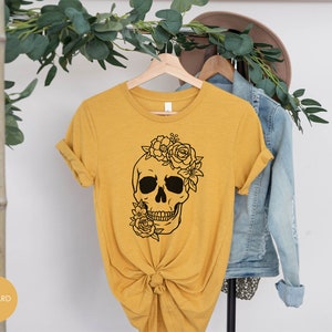 Peut inclure: Un t-shirt jaune moutarde avec un motif de cr&acirc;ne floral noir. Le cr&acirc;ne porte une couronne florale.