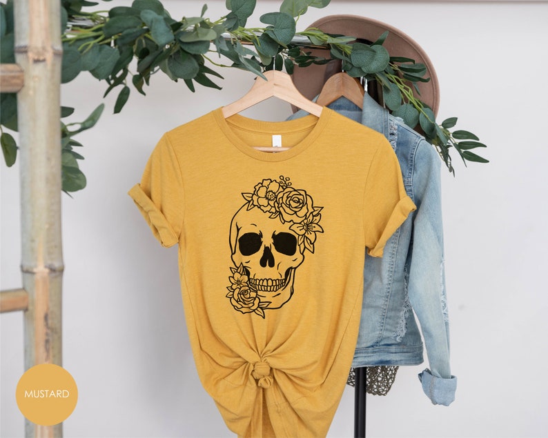 Peut inclure: Un t-shirt jaune moutarde avec un motif de cr&acirc;ne floral noir. Le cr&acirc;ne porte une couronne florale.