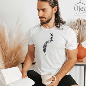Op de afbeelding: Een wit T-shirt met een zwart-witte afbeelding van een veer met vogels die er vanaf vliegen. De afbeelding is gecentreerd op het T-shirt.