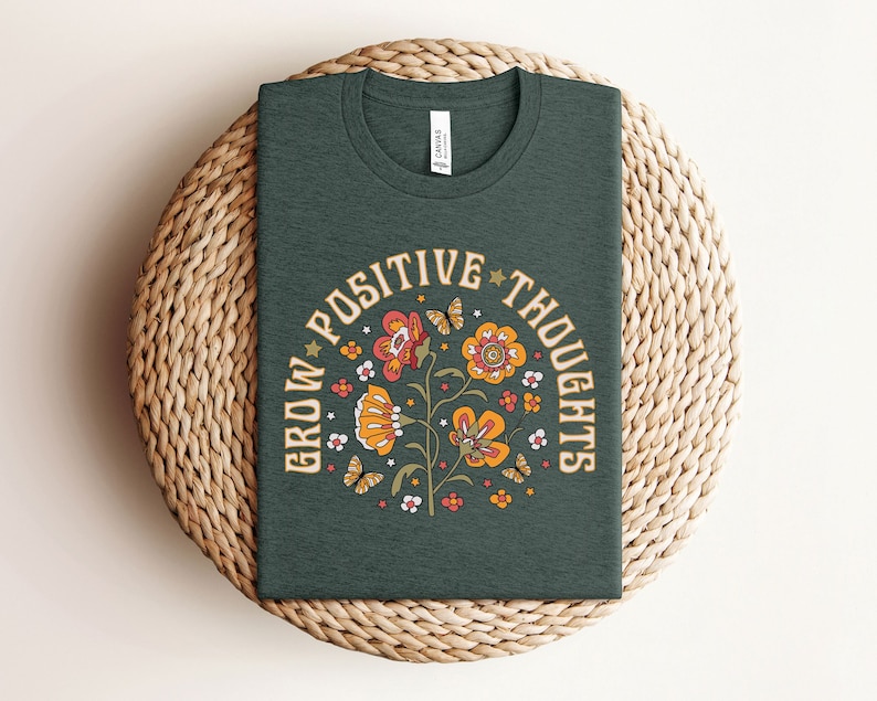 May include: A dark green t-shirt with a floral design and the text "Grow Positive Thoughts" in a retro font.