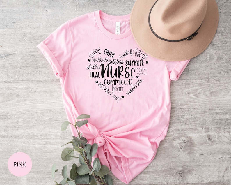 May include: Pink t-shirt with a black graphic design that says "Strong, Care, Tough, Kind, Nurture, Selfless, Support, Skilled, Nurse, Respect, Heal, Committed, Heart, Encourage, Compassion".