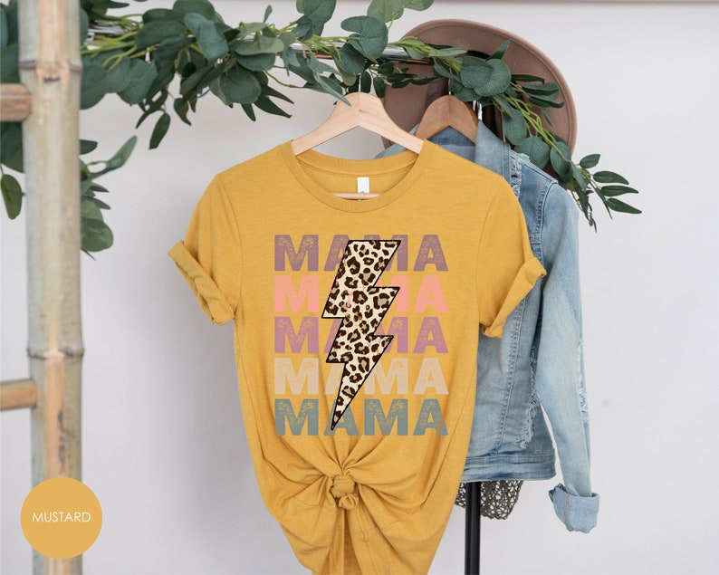 Op de afbeelding: Een mosterdgeel T-shirt met een bliksemgraphic in luipaardprint en de tekst "MAMA" die in verschillende kleuren wordt herhaald.