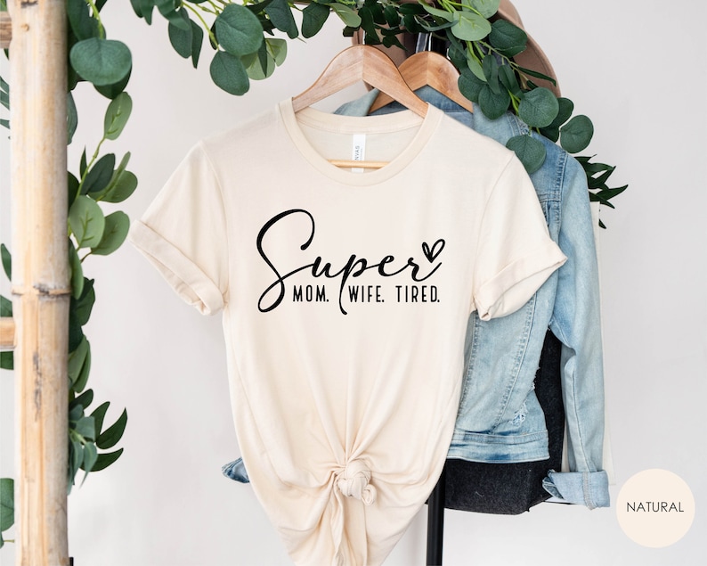 May include: A beige t-shirt with the text "Super Mom. Wife. Tired." in black cursive lettering and a small heart.