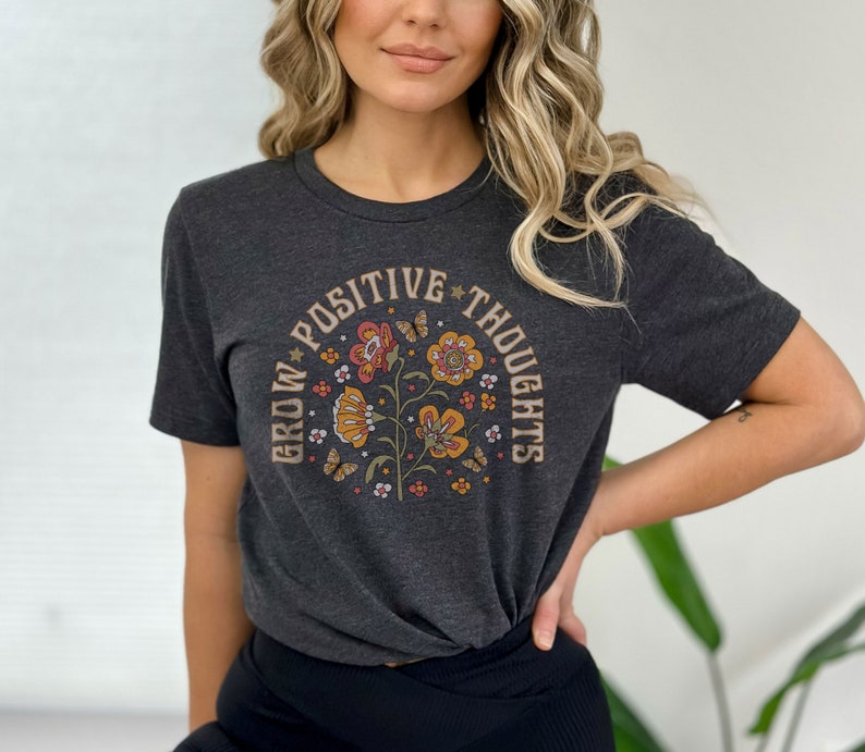 May include: A dark grey t-shirt with a floral design and the text "Grow Positive Thoughts" in a circle around the flowers.