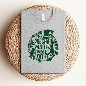 May include: A gray t-shirt with a green graphic that says "The Leprechauns Made Me Do It". The graphic features a leprechaun with a hat and a pot of gold.