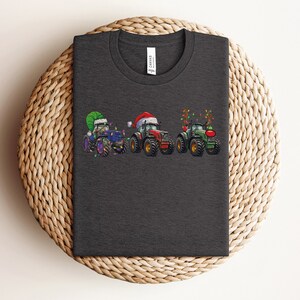 Peut inclure: Un t-shirt gris fonc&eacute; avec un motif de trois tracteurs d&eacute;cor&eacute;s pour No&euml;l. Les tracteurs sont vert, bleu et rouge. Les tracteurs portent des chapeaux de P&egrave;re No&euml;l et ont des lumi&egrave;res de No&euml;l.